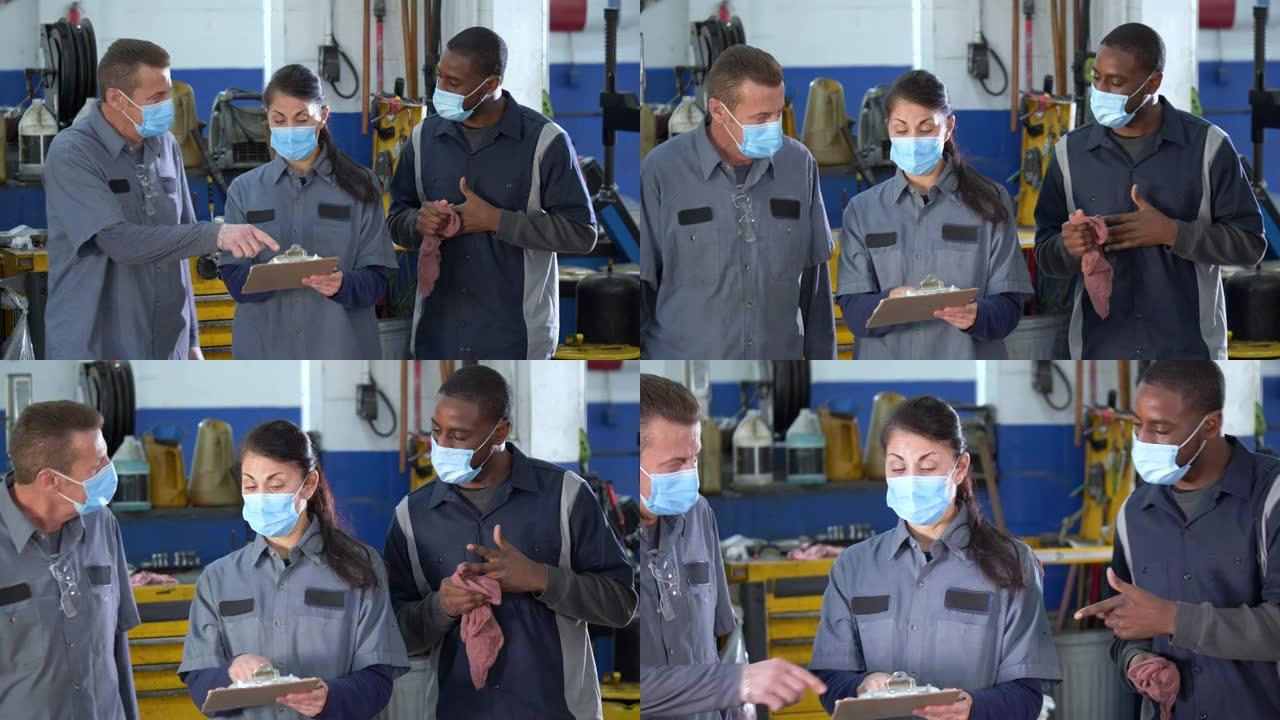 机械师在汽车修理厂交谈，戴着口罩