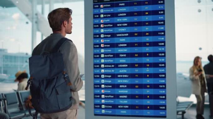 机场航站楼: 年轻人看着到达和离开信息显示，寻找他的航班。背景: 不同的人群在航空枢纽的登机休息室等