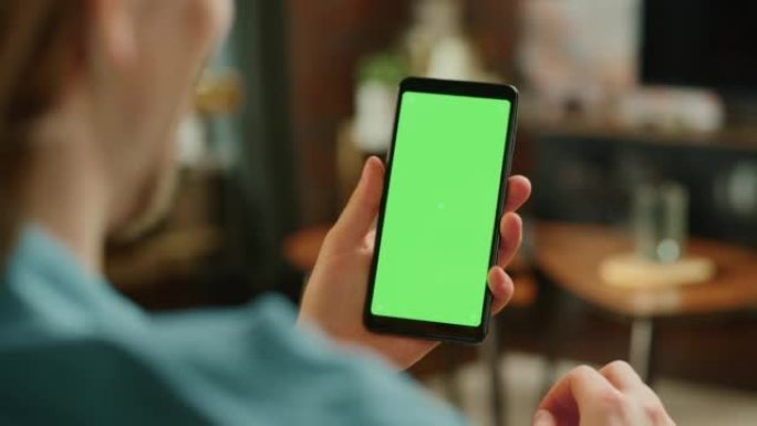 带有绿屏模拟显示的智能手机上的Man滚动供稿。男性在家里休息时在移动设备上享受社交媒体上的乐趣和内容