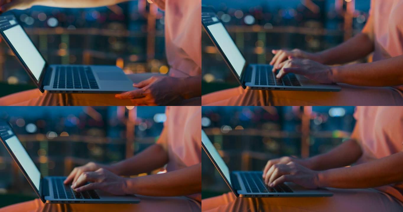 年轻女子的手在城市之夜使用笔记本电脑