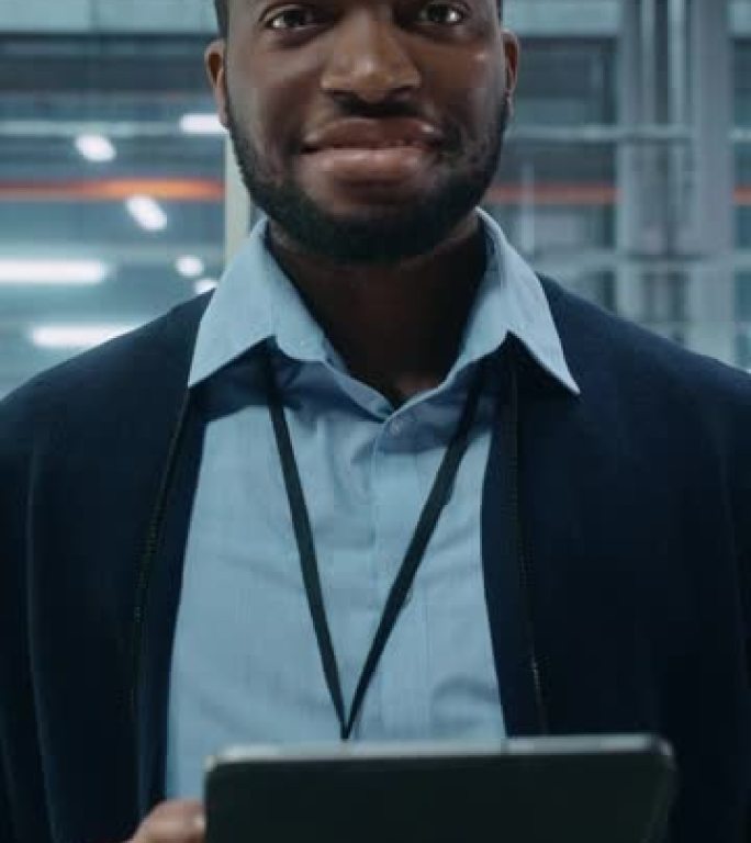 垂直屏幕。汽车厂办公室: 黑人男性总工程师的肖像在自动化机器人手臂装配线上使用平板电脑制造高科技电动