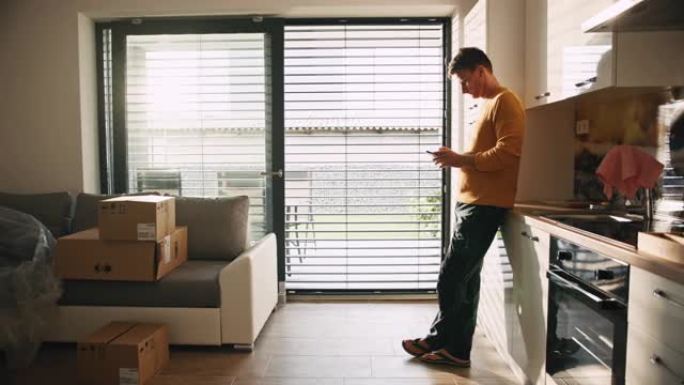 男子在他的新公寓里从冰箱里拿出啤酒罐时打开百叶窗并使用手机