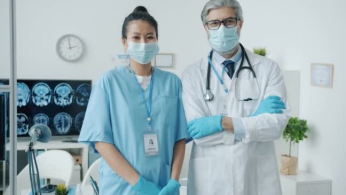 穿着磨砂膏的护士和穿着白色长袍的医生站在诊所办公室的慢动作肖像