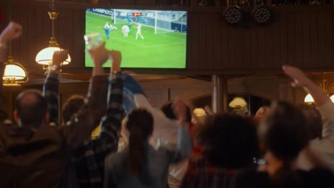 一群足球迷在体育酒吧观看现场足球比赛。人们站在电视机前，为他们的团队欢呼。球员进球，人群庆祝赢得冠军