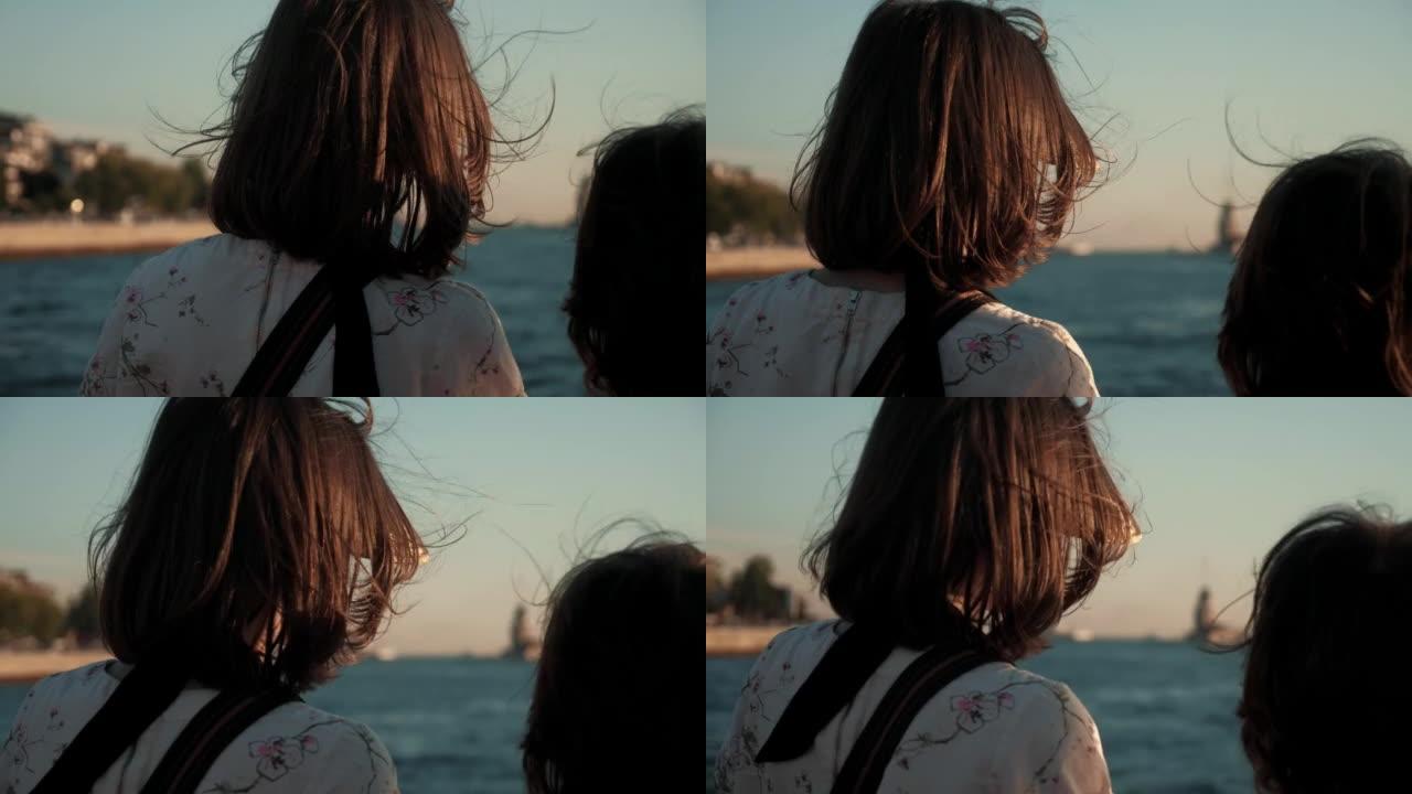 令人惊叹的电影后视，快乐的十几岁的女孩和男孩，风吹着头发，在海上游轮上观看日落景色。