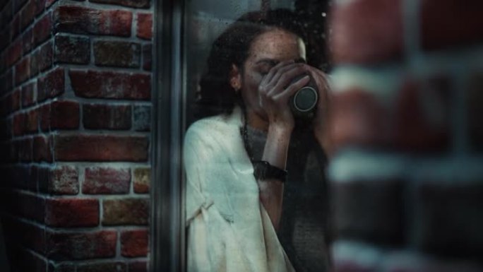 悲伤的女人心情忧郁，感到沮丧。绝望的拉丁女性坐在窗台上，在雨中的街道上看着窗外。孤独概念。公寓窗户内