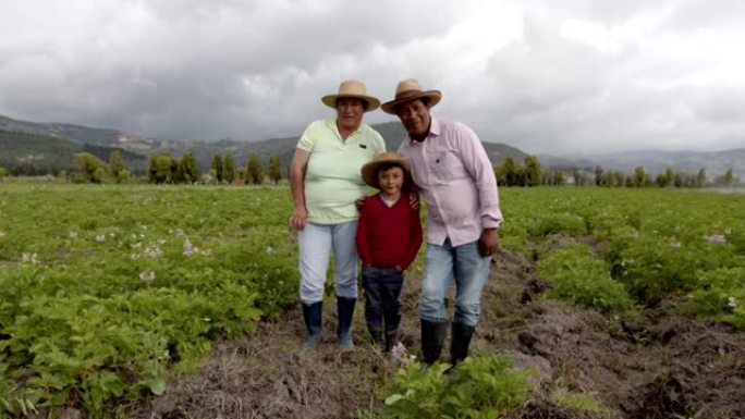 美丽的拉丁美洲农民家庭在马铃薯收割场站在一起，对着镜头微笑