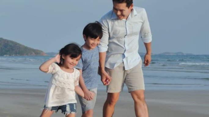 亚洲父亲与男孩和女孩的幸福家庭，年龄在4-8岁之间，手牵手，在沙滩上沿着大海的边缘奔跑。活跃的父母和
