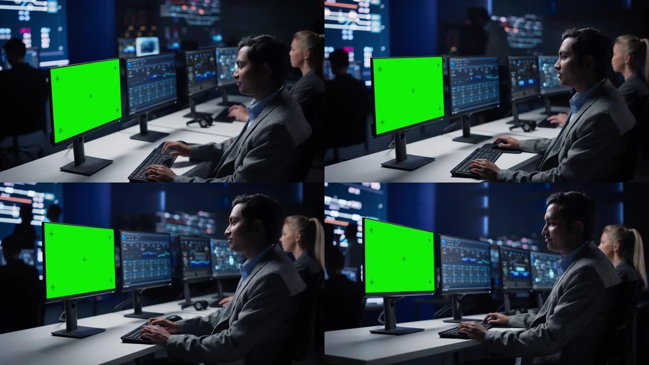 自信的男性数据科学家在大型基础设施控制室的绿色色度键屏幕计算机上工作。专家使用显示图表、信息的计算机