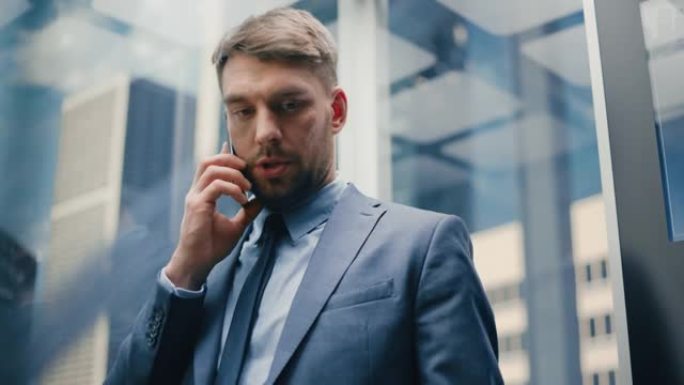 成功的商人穿着西装骑着玻璃电梯到现代商务中心的办公室。英俊严肃的男人在打电话，在电梯里接一个重要的商