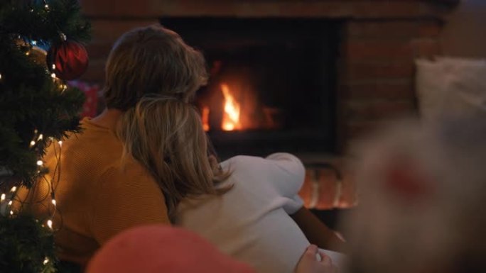 圣诞假期期间，SLO MO DS年轻夫妇坐在壁炉前拥抱