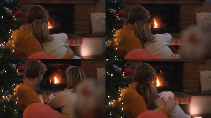 圣诞假期期间，SLO MO DS年轻夫妇坐在壁炉前拥抱
