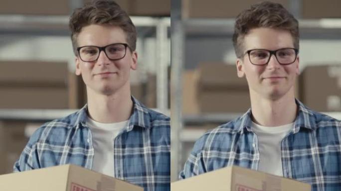 垂直屏幕: 一个成功的年轻小企业主微笑着看着相机的肖像。高加索男性在仓库储藏室里拿着一个纸板箱，订单