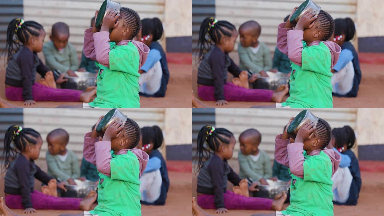 非洲的贫困。年轻的饥饿黑人非洲女孩从锅里吃玉米，三个孩子在背景中