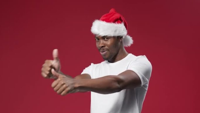 一个戴着圣诞帽和白色t恤的皮肤黝黑的男人笑容灿烂，竖起大拇指
