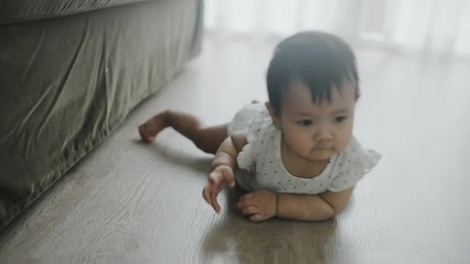 亚洲婴儿在家里木地板上的肚子上爬行。