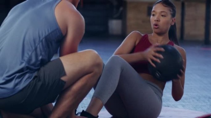活跃的女人在健身房健身教练的帮助下锻炼时，用加重的球进行俄罗斯扭曲。年轻运动员在核心和腹肌锻炼期间保