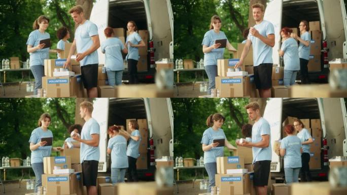 在阳光明媚的日子里，一组年轻的志愿者在面包车中准备人道主义援助口粮，食物，捐赠和装载包裹。慈善工作者