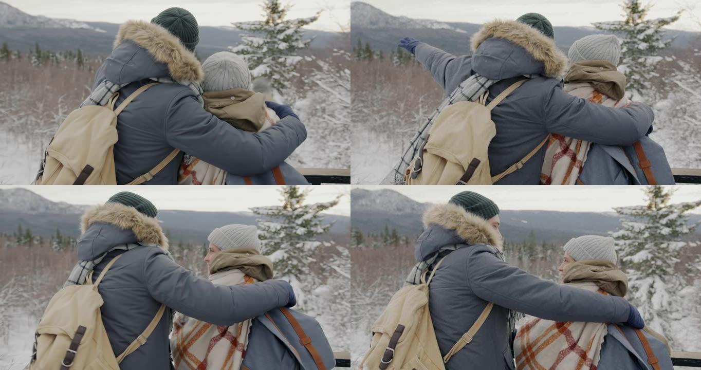 幸福的年轻夫妇享受着美丽的景色，指着冬天的山脉聊天