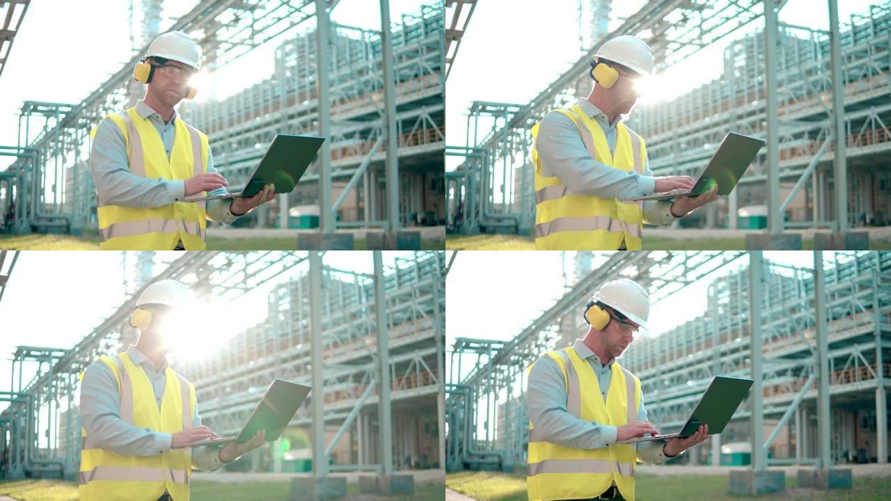 戴着安全帽和耳机的炼油厂工程师正在现代工业设施中操作笔记本电脑