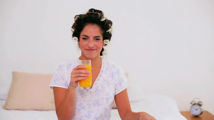 穿着卷发器享受橙汁的快乐女人
