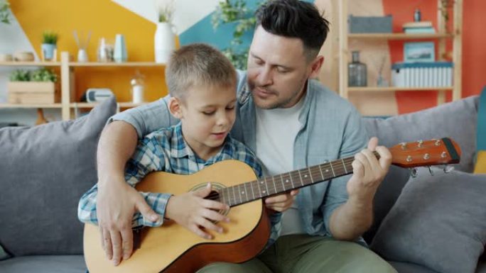 可爱的男孩在关心父亲的指导下弹吉他在家学习