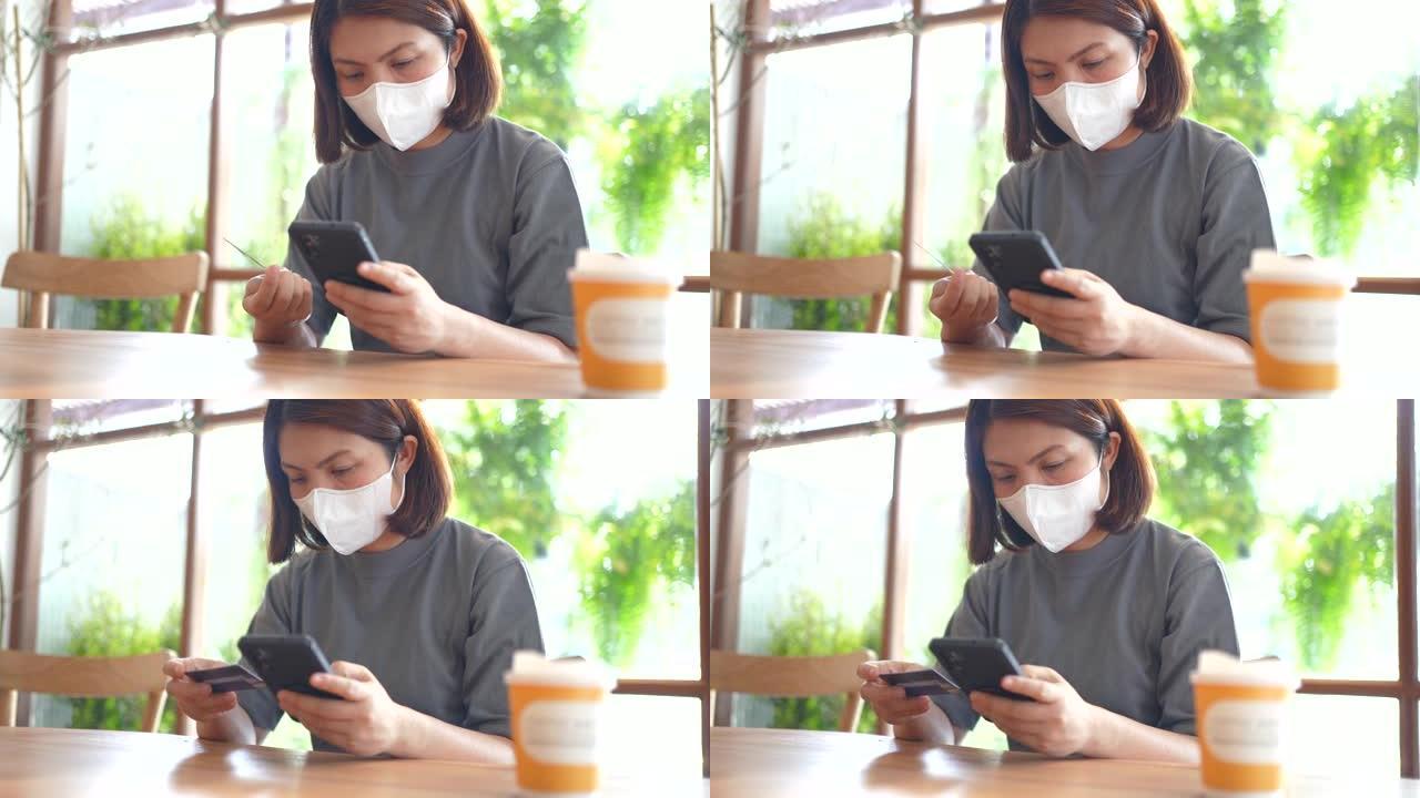 用信用卡支付智能手机的女人在咖啡馆戴着新的普通口罩