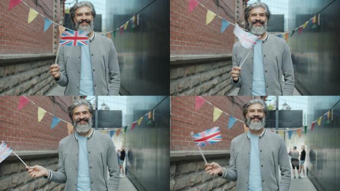 快乐的成熟英国人的慢动作挥舞着英国国旗，微笑着站在街上