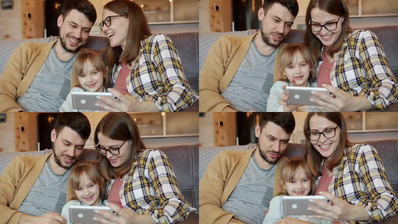 快乐的人母亲父亲和女儿使用智能手机看着屏幕并在家里大笑