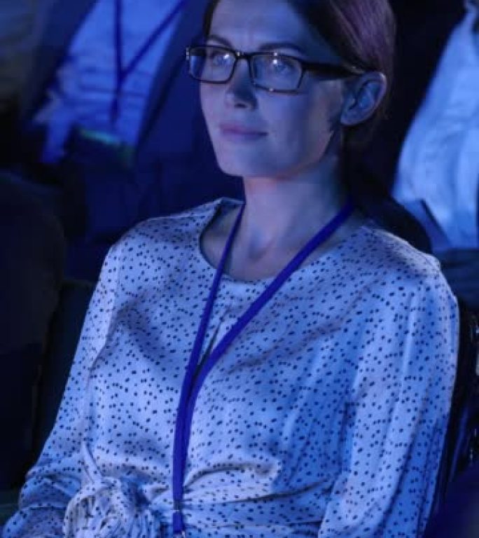 垂直屏幕: 女性坐在科技会议上黑暗拥挤的礼堂里。使用笔记本电脑的年轻女子。关于新软件和高科技产品的专