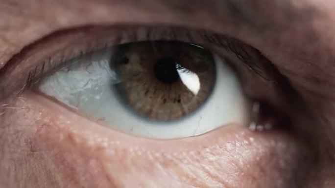 老人的眼睛看着侧面，近距离拍摄。睫毛老化眼睑下真实虹膜和瞳孔的宏观缩放图像。户外成熟老年人的角膜和视