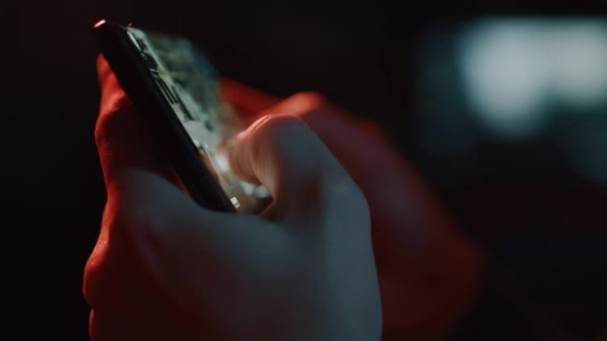 一个年轻的游戏玩家的电影特写镜头正在使用智能手机播放隔离在黑暗背景上的最新创新技术视频游戏。
