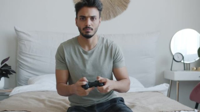 兴奋的阿拉伯男子喜欢独自玩电子游戏并看着相机的肖像