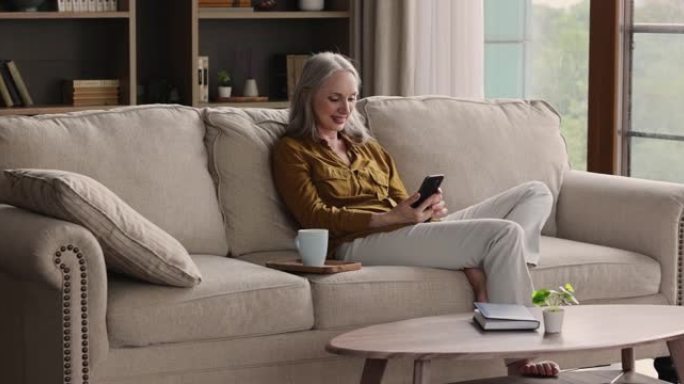 微笑的60多岁老太太用智能手机在沙发上放松
