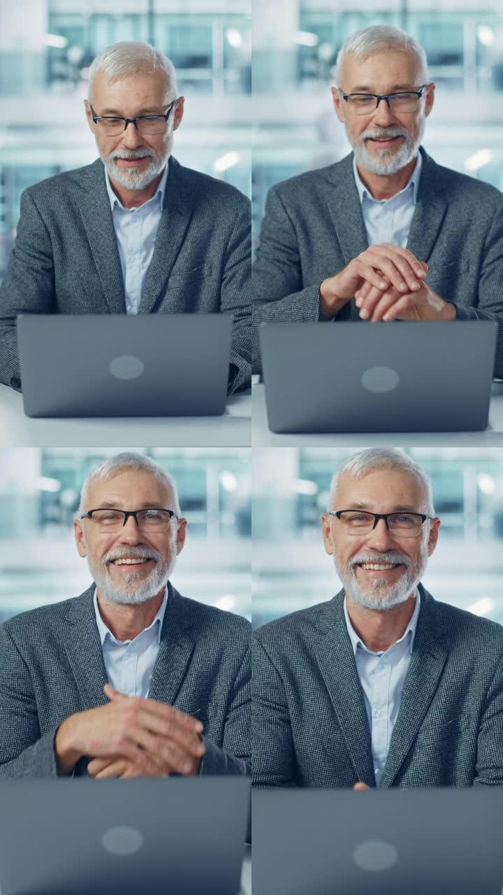 垂直视频。现代办公室: 成功的中年大胡子商人在办公桌前的笔记本电脑上工作的肖像。微笑的企业工人。拥有