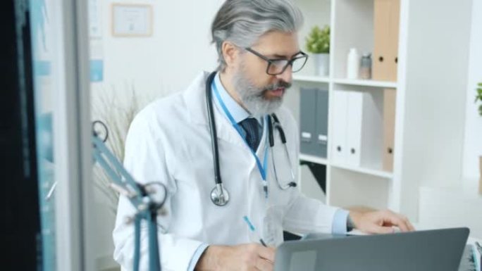 成熟的医生在办公室使用笔记本电脑进行在线视频咨询时讨论MRI扫描