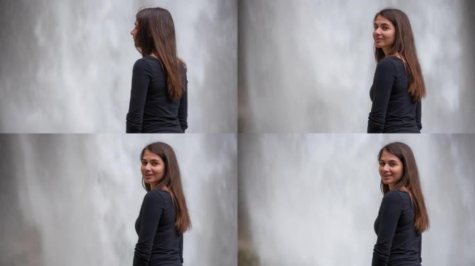 年轻女子站在瀑布前回头微笑