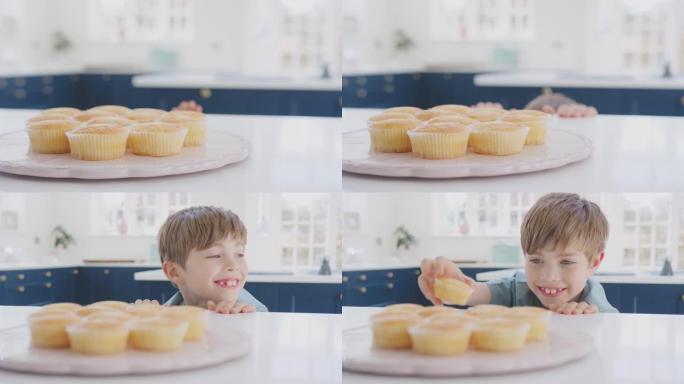 男孩的特写镜头从家里厨房的盘子里拿出新鲜出炉的自制纸杯蛋糕