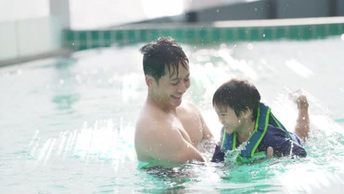 夏季，年轻的亚洲父子在阳光照射下的游泳池里游泳