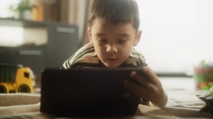 缓慢放大: 一个使用数字平板电脑的亚洲男孩子的肖像，在他的房间里微笑。可爱的小男孩享受周末，玩教育游