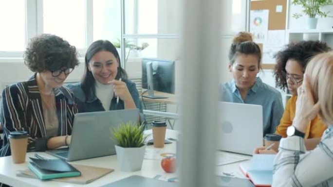 快乐的女企业家在玻璃墙办公室里交流和使用电脑