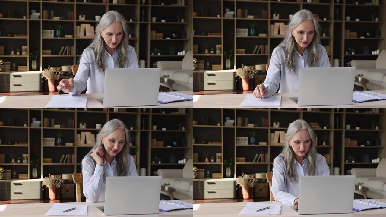 年长的女商人坐在办公桌前检查笔记本电脑上的文件