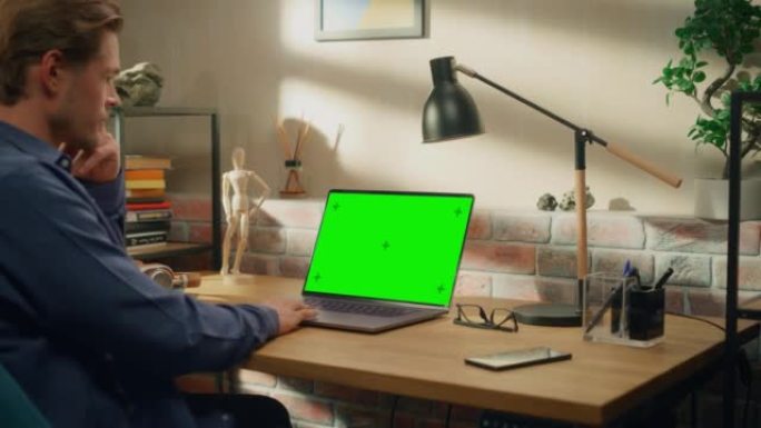 年轻英俊的男人在家工作，手提电脑上有绿屏模拟显示。创意男性查看社交媒体，浏览互联网。明亮阁楼公寓的客