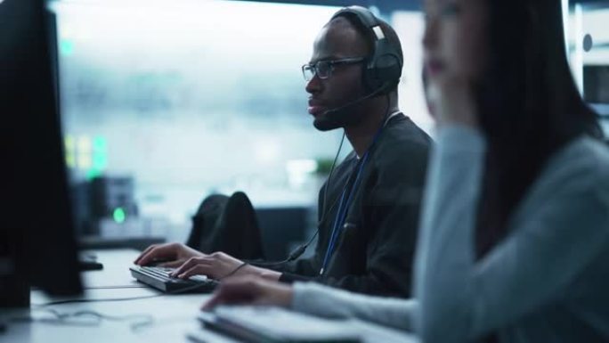 在技术初创公司服务台部门工作的聪明的非洲年轻专家的肖像，在多元化的办公室中使用计算机。黑人男子戴眼镜
