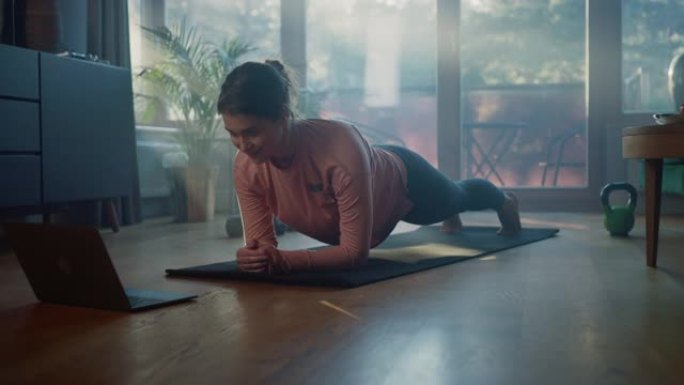 漂亮的女孩在家锻炼，在笔记本电脑上看教程。正宗的大码女性做日常运动、健身锻炼、木板、伸展瑜伽练习。阳