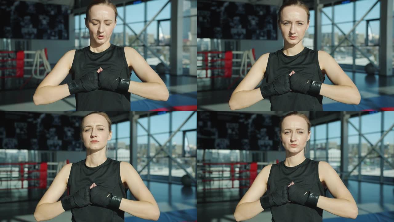 美丽的年轻女运动员的肖像，双手裹着站在健身房看着相机