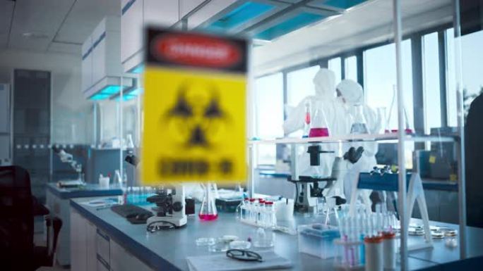病毒学和医学研究实验室玻璃门上的危险新型冠状病毒肺炎标志: 戴着口罩和工作服的科学家团队致力于新型冠
