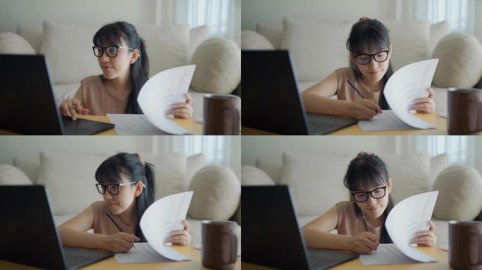 在家庭办公室使用笔记本电脑和阅读文书工作的年轻亚洲女性的特写镜头。