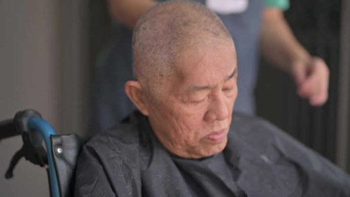 坐在轮椅上的亚洲华裔高级男子在他家前院理发