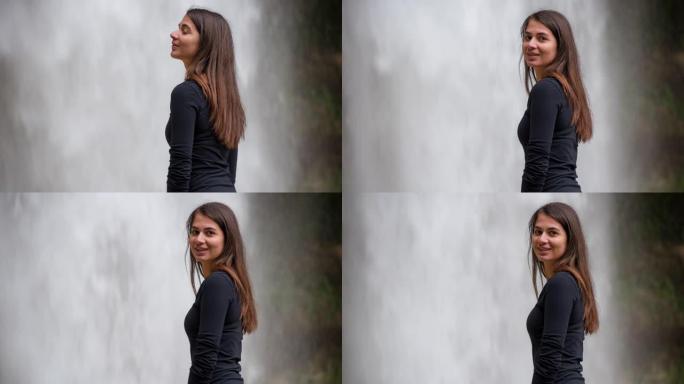年轻女子站在瀑布前的边缘回头微笑